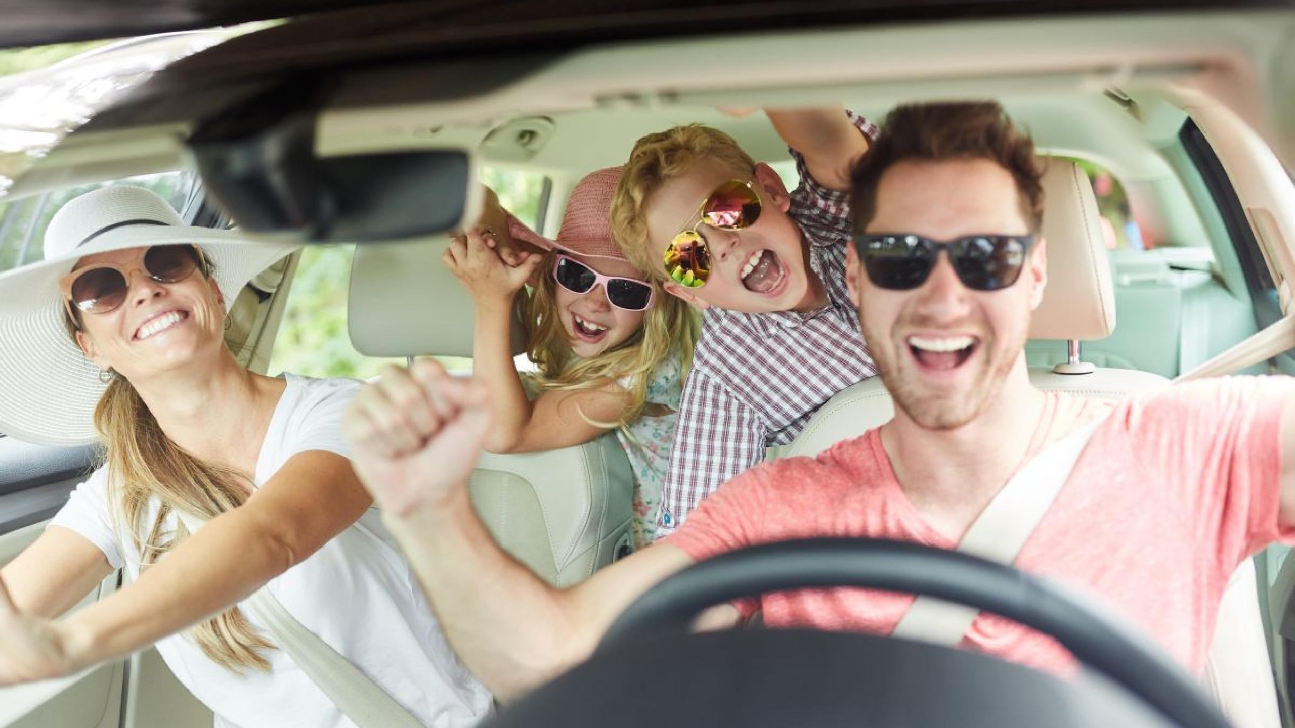 Vrolijk gezin met twee kinderen in vakantiestemming in de auto.