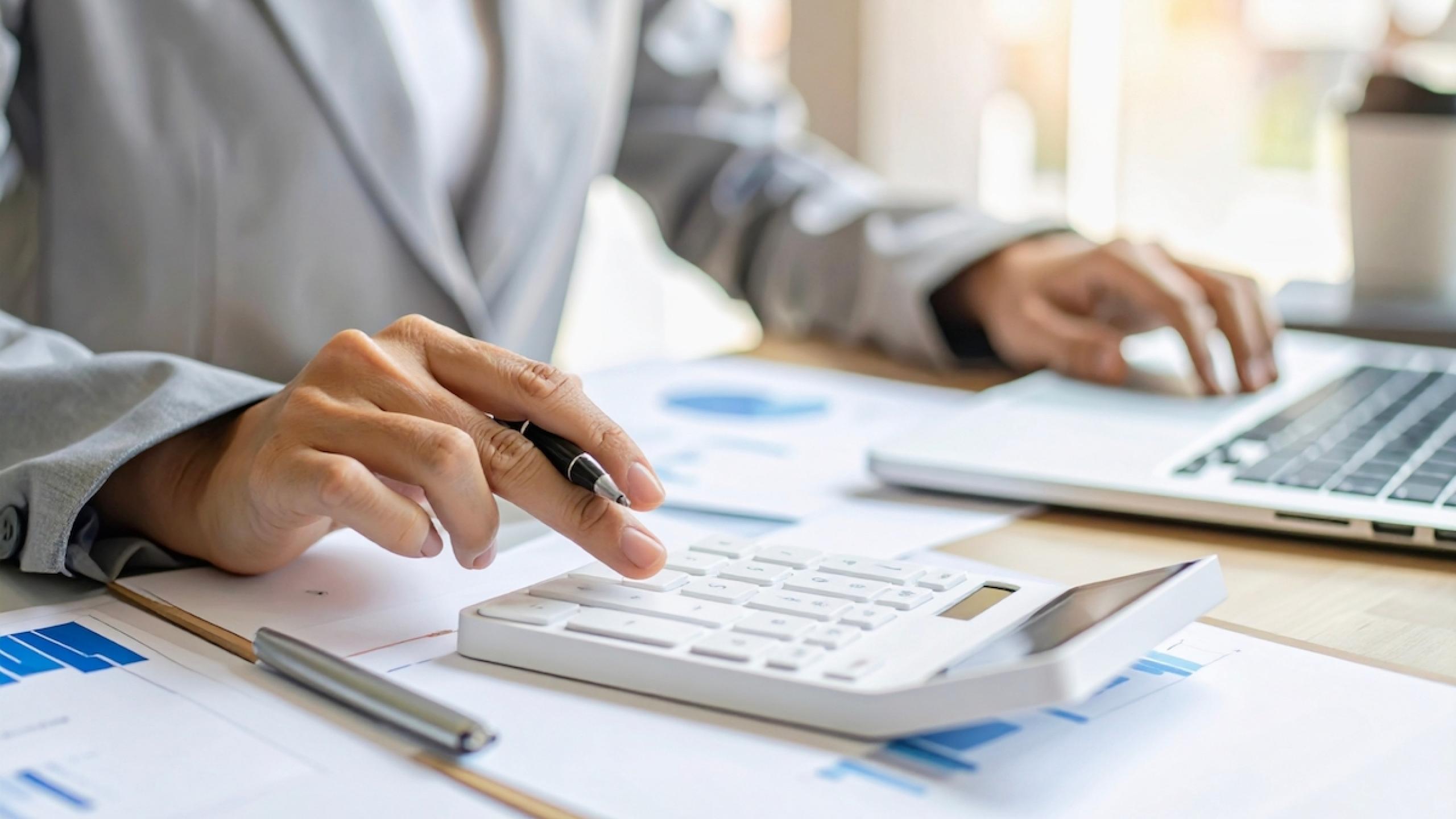 Close-up handen met rekenmachine en laptop.